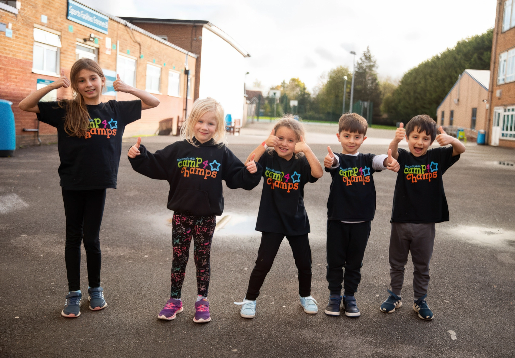 Children in Camp 4 Champs tops giving thumbs up outside a school holiday camp venue